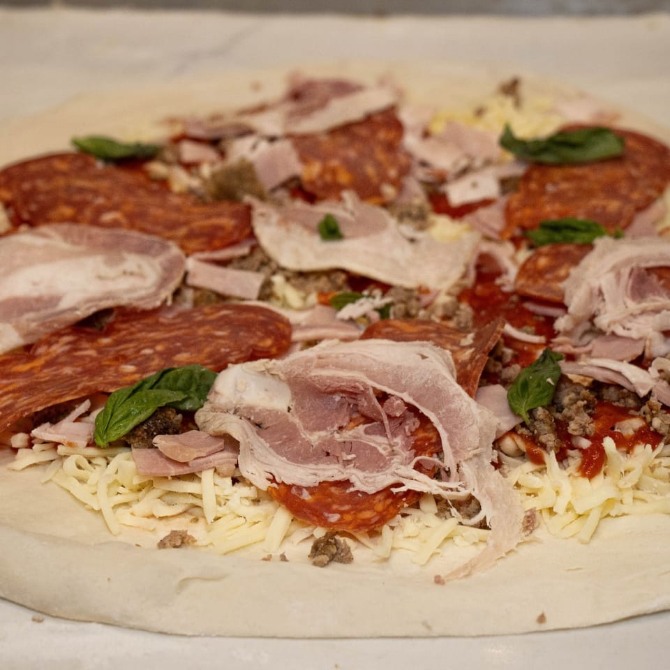 Pizza topped with meats and basil before baking.
