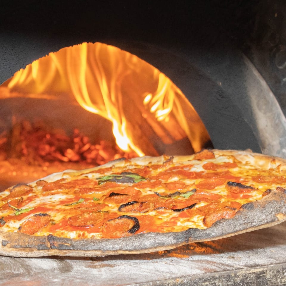 Freshly baked pizza being lifted from the wood-fired oven.