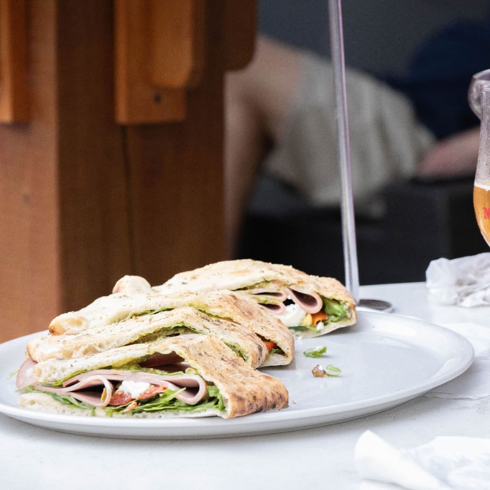 Wood-fired sandwich served on a plate beside a beer.