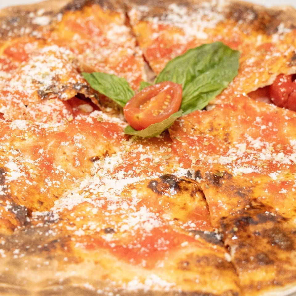 Wood-fired tomato pizza with fresh basil, cherry tomato, and grated cheese.