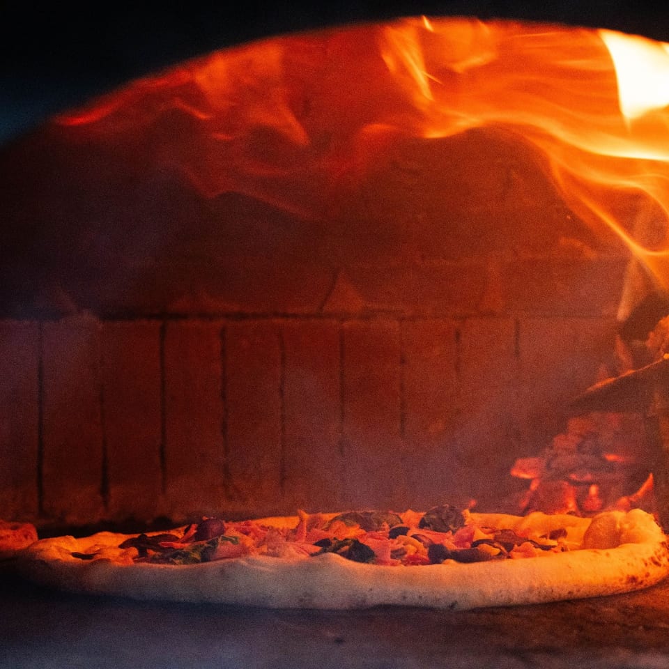 Pizzas baking beside flames inside the wood-fired oven.