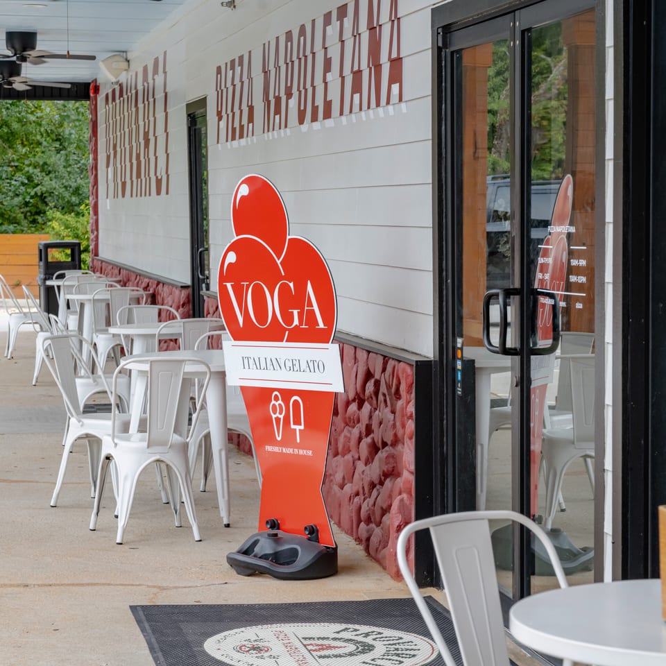 Voga Italian Gelato storefront with outdoor white café tables, chairs, and a red gelato sign beneath a covered patio.